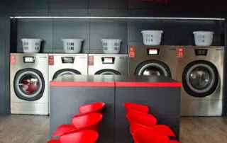 Washing machines positioned in front of a vibrant red chairs, showcasing a modern laundry setup in a stylish interior.
