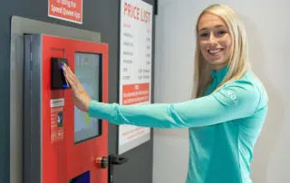 A woman in a green shirt stands beside a red machine, showcasing a contrast of colors in the industrial setting.